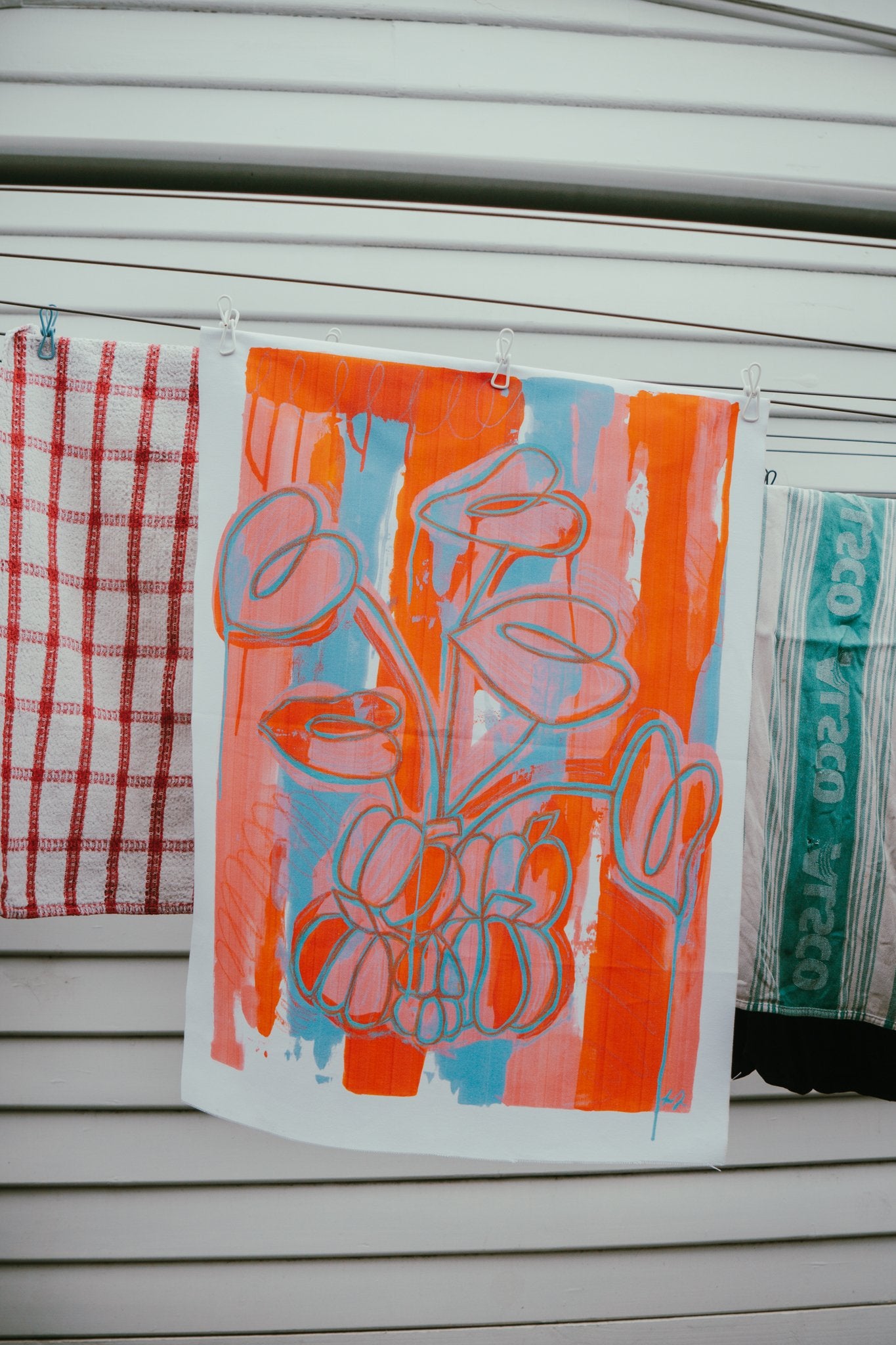 Tea towels by Jay-Dee Pitcaithly with floral design hanging on a washing line.